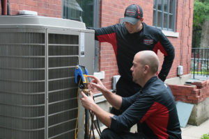 Two Northern Comfort System technicians performing maintenance on AC unit