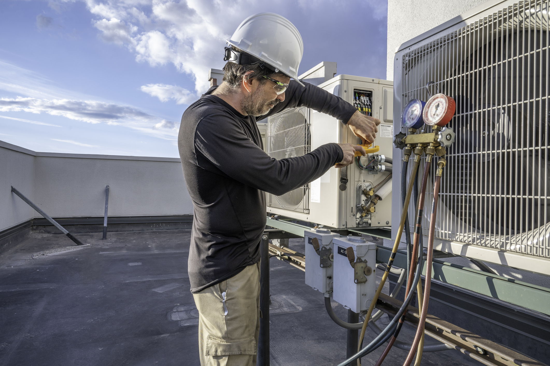 HVAC technician servicing a ductless mini-split outdoor unit on the roof of a commercial building.